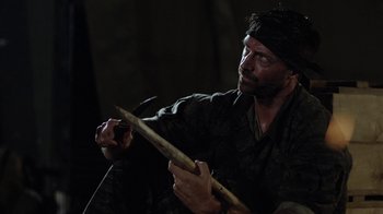 Movie still from “Oats Studios” (2017), directed by Neill Blomkamp – A man holding a wooden stick while sitting on a chair; Close Up shot, Over the shoulder angle