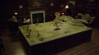 Movie still from “Oats Studios” (2017), directed by Neill Blomkamp – A room with a table and a fire place in the background; Extreme Wide shot, High angle