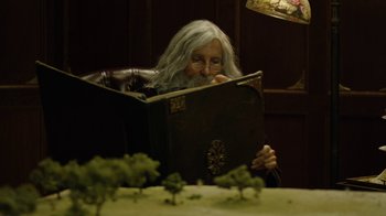 Movie still from “Oats Studios” (2017), directed by Neill Blomkamp – An old woman reading a book in a dark room; Medium shot, High angle