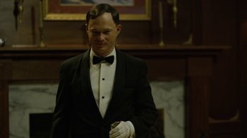 Movie still from “Oats Studios” (2017), directed by Neill Blomkamp – A man in a suit and bow tie standing in front of a fireplace; Medium shot, Low angle