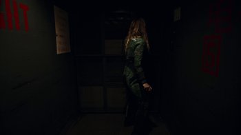 Movie still from “Oats Studios” (2017), directed by Neill Blomkamp – A woman in a green suit standing in a dark room; Wide shot, High angle