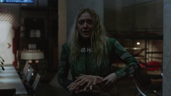 Movie still from “Oats Studios” (2017), directed by Neill Blomkamp – A woman in a green outfit holding her hands; Medium shot, Over the shoulder angle