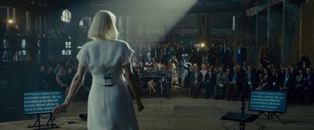 Movie still from “Okja” (2017), directed by Bong Joon Ho – A woman in a white dress standing in front of an audience; Wide shot, Over the shoulder angle