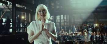 Movie still from “Okja” (2017), directed by Bong Joon Ho – A woman with blonde hair and a white dress is holding her hands together; Medium shot, Over the shoulder angle