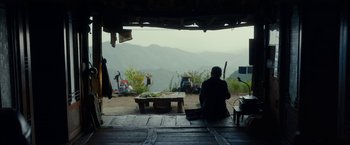 Movie still from “Okja” (2017), directed by Bong Joon Ho – A man sitting on the ground in front of a table; Extreme Wide shot, Over the shoulder angle
