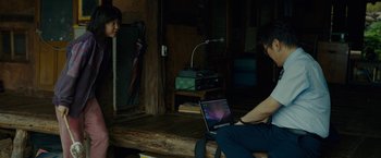 Movie still from “Okja” (2017), directed by Bong Joon Ho – A man sitting on top of a wooden bench next to another man; Medium shot, Over the shoulder angle