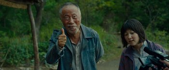 Movie still from “Okja” (2017), directed by Bong Joon Ho – An older man giving a thumbs up while standing on a path; Medium shot, Low angle