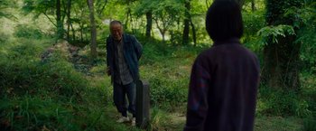 Movie still from “Okja” (2017), directed by Bong Joon Ho – An older man standing next to a grave in a forest; Medium shot, Over the shoulder angle