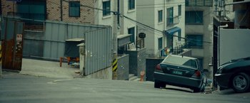 Movie still from “Okja” (2017), directed by Bong Joon Ho – A car driving down a street next to a building; Wide shot, Low angle