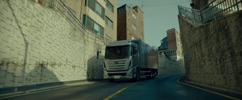 Movie still from “Okja” (2017), directed by Bong Joon Ho – A truck driving down a street next to tall buildings; Extreme Wide shot, Low angle