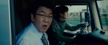 Movie still from “Okja” (2017), directed by Bong Joon Ho – Two men driving in a car in the back of a vehicle; Close Up shot, Over the shoulder angle