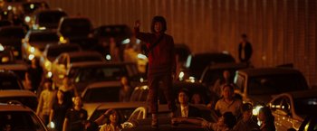 Movie still from “Okja” (2017), directed by Bong Joon Ho – A person standing on top of a car at night; Wide shot, Low angle
