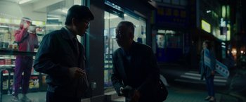 Movie still from “Okja” (2017), directed by Bong Joon Ho – Two men are talking in the dark outside a store; Medium shot, Over the shoulder angle