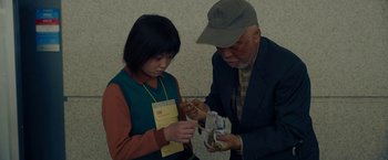 Movie still from “Okja” (2017), directed by Bong Joon Ho – An older man and a young girl looking at a package; Medium shot, High angle