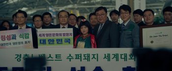 Movie still from “Okja” (2017), directed by Bong Joon Ho – A group of people standing next to each other in front of a sign; Medium shot, Over the shoulder angle