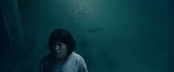 Movie still from “Okja” (2017), directed by Bong Joon Ho – A woman in white shirt sitting in front of a wall; Close Up shot, High angle