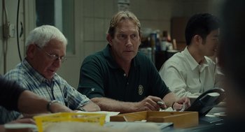 Movie still from “Moneyball” (2011), directed by Bennett Miller – A man sitting at a table in front of two other men; Medium shot, Over the shoulder angle