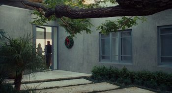 Movie still from “Moneyball” (2011), directed by Bennett Miller – A person standing in front of a building with a christmas wreath on the wall; Wide shot, Over the shoulder angle