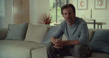 Movie still from “Moneyball” (2011), directed by Bennett Miller – A man sitting on top of a couch in a living room; Medium shot, Over the shoulder angle