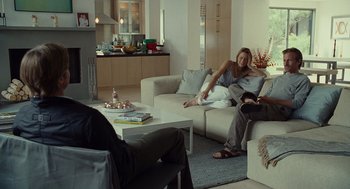 Movie still from “Moneyball” (2011), directed by Bennett Miller – Two people are sitting on a couch in a living room; Wide shot, Over the shoulder angle