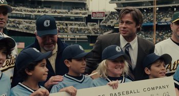 Movie still from “Moneyball” (2011), directed by Bennett Miller – A group of young boys and a man in a baseball uniform; Medium shot, Over the shoulder angle