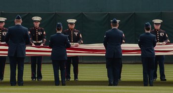 Movie still from “Moneyball” (2011), directed by Bennett Miller – A group of men in uniform standing next to an american flag; Wide shot, Low angle