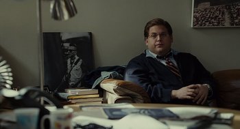 Movie still from “Moneyball” (2011), directed by Bennett Miller – A man sitting on a couch in front of some books; Medium shot, Over the shoulder angle