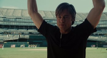 Movie still from “Moneyball” (2011), directed by Bennett Miller – A man in a black t - shirt holds his arm up in the air; Medium shot, Low angle