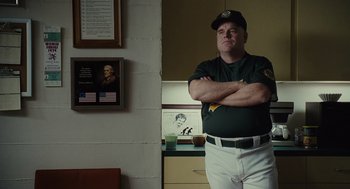 Movie still from “Moneyball” (2011), directed by Bennett Miller – A man in a baseball uniform standing with his arms crossed; Medium shot, Over the shoulder angle