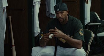 Movie still from “Moneyball” (2011), directed by Bennett Miller – A baseball player sitting in the locker room holding a baseball bat; Medium shot, Over the shoulder angle