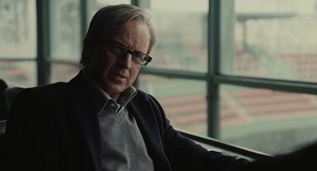 Movie still from “Moneyball” (2011), directed by Bennett Miller – An older man wearing glasses sitting in front of a window; Close Up shot, Over the shoulder angle