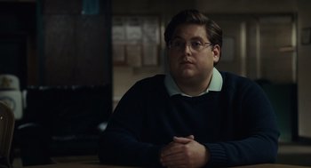 Movie still from “Moneyball” (2011), directed by Bennett Miller – A man sitting at a table with his arms crossed; Close Up shot, Over the shoulder angle