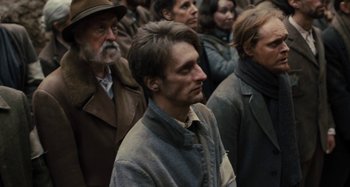 Movie still from “Operation Finale” (2018), directed by Chris Weitz – A group of people standing around each other in a crowd; Medium shot, Over the shoulder angle