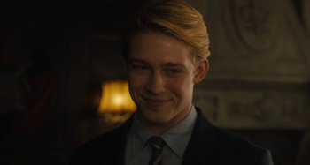 Movie still from “Operation Finale” (2018), directed by Chris Weitz – A man in a suit and tie smiling for the camera; Close Up shot, Over the shoulder angle