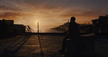 Movie still from “Operation Finale” (2018), directed by Chris Weitz – A man sitting on top of a bench near the ocean; Extreme Wide shot, High angle
