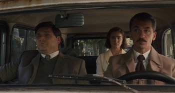 Movie still from “Operation Finale” (2018), directed by Chris Weitz – A man and a woman in a car with another man in the back seat; Medium shot, Over the shoulder angle