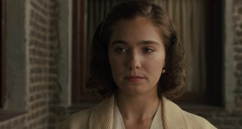 Movie still from “Operation Finale” (2018), directed by Chris Weitz – A young woman in a white jacket looking at the camera; Close Up shot, Over the shoulder angle