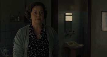 Movie still from “Operation Finale” (2018), directed by Chris Weitz – An older woman standing in a bathroom next to a sink; Medium shot, Over the shoulder angle