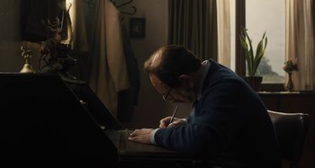 Movie still from “Operation Finale” (2018), directed by Chris Weitz – A man sitting at a desk writing on a piece of paper; Medium shot, High angle