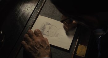 Movie still from “Operation Finale” (2018), directed by Chris Weitz – A person drawing a picture of a man with glasses; Extreme Close Up shot, High angle