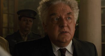 Movie still from “Operation Finale” (2018), directed by Chris Weitz – An older man in a suit and tie looking surprised; Close Up shot, Over the shoulder angle