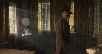 Movie still from “Operation Finale” (2018), directed by Chris Weitz – A man in a hat and a coat standing in a room; Wide shot, Low angle
