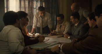 Movie still from “Operation Finale” (2018), directed by Chris Weitz – A group of people sitting around a table with papers on top of it; Medium shot, High angle