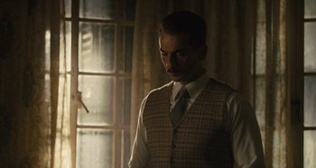Movie still from “Operation Finale” (2018), directed by Chris Weitz – A man in a vest and tie standing next to a window; Medium shot, Low angle