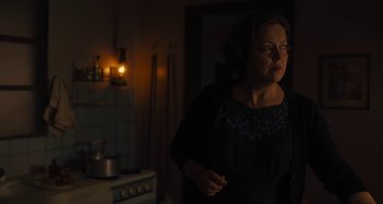 Movie still from “Operation Finale” (2018), directed by Chris Weitz – A woman standing in the dark in front of a stove; Medium shot, Over the shoulder angle