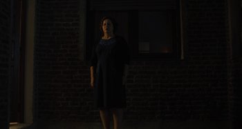 Movie still from “Operation Finale” (2018), directed by Chris Weitz – A woman standing in the dark in front of a brick wall; Medium shot, Low angle