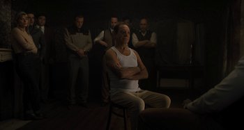Movie still from “Operation Finale” (2018), directed by Chris Weitz – A man sitting in a chair with his arms crossed; Medium shot, Over the shoulder angle