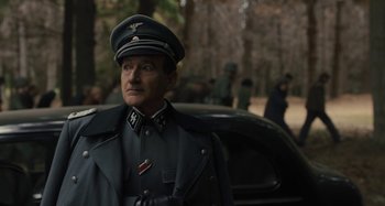 Movie still from “Operation Finale” (2018), directed by Chris Weitz – A man in a military uniform standing in front of a car; Medium shot, Over the shoulder angle
