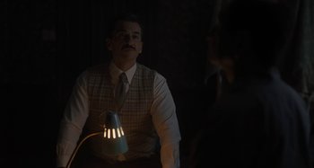 Movie still from “Operation Finale” (2018), directed by Chris Weitz – A man sitting in a dark room with a lamp in his hand; Medium shot, Over the shoulder angle