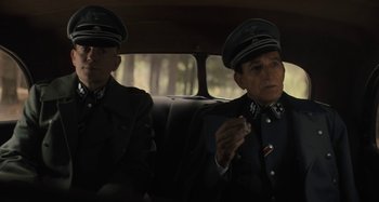 Movie still from “Operation Finale” (2018), directed by Chris Weitz – Two men in uniforms sitting in a car; Medium shot, Over the shoulder angle